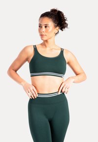 Ciemnozielony sportowy biustonosz z podwójnymi ramiączkami i białym paskiem w paski. Do kompletu ciemnozielone legginsy z wysokim stanem. Gładka tekstura.