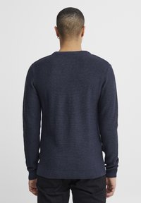 Pulover tricotat de culoare albastru marin, cu guler rotund și manșete și tiv cu nervuri. Textura are un model orizontal subtil. Vedere din spate.