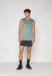 Lichtgroen mouwloos sportshirt met een zwart logo, gecombineerd met donkere, gestructureerde shorts en zwarte sportschoenen.