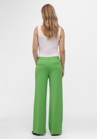 Pantalones verdes de pierna ancha con una cinturilla elástica y dos bolsillos traseros. Combinados con una camiseta sin mangas blanca, que muestra una textura suave y ajustada.