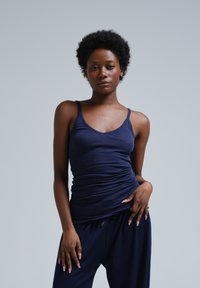 Navy blue fitted tank top with thin straps, featuring gathered detailing at the waist, paired with relaxed navy pants. Smooth texture.