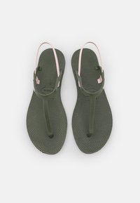 Green rubber sandals with a textured sole, featuring thin pink straps. The design includes a classic thong style and subtle branding.