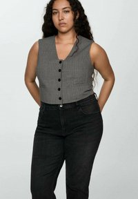 Sivo prugasto kratko telovnik s V-izrezom, z črnimi gumbi po sprednji strani. Nosi se z visokim pasom črnimi kavbojkami.