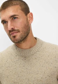 Beige Strickpullover mit geripptem Rundhalsausschnitt; melierter Stoff mit kleinen Flecken in Braun und Blau; weicher, mittelschwerer Stoff.