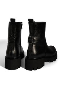 Bottines noires en cuir avec une finition texturée, dotées de fermetures éclair sur les côtés et d'accents de boucle en métal sur le talon. Semelle épaisse et robuste en noir.
