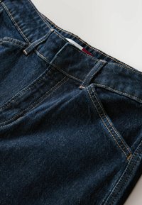 Tumerohelised teksapüksid kollase õmblusega, millel on klassikaline viie taskuga disain ja sirge lõikega siluett. Detailidena on kasutatud naelu.