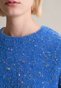 Blauer strukturierter Pullover mit rundem Ausschnitt. Mit bunten Sprenkeln in Gelb, Pink und Orange auf einem weichen, flauschigen Stoff.