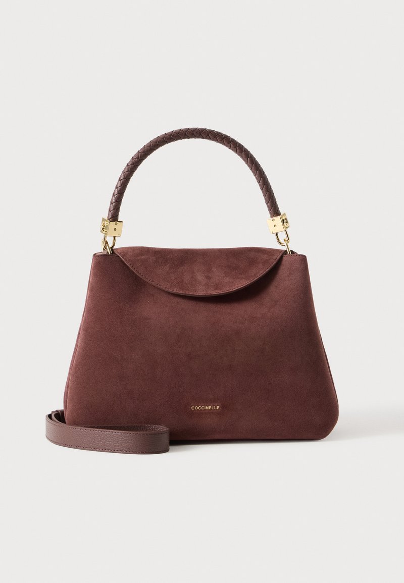 Sac à main en daim marron avec poignée supérieure tressée, bandoulière amovible, quincaillerie dorée et petit logo « Coccinelle » sur le devant.