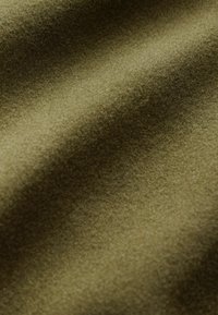 Tissu vert olive doux avec une texture lisse, légèrement duveteuse et des plis délicats créant des ombres et des reflets.