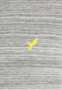 Maglione grigio a maglia con un tessuto testurizzato caratterizzato da un logo di uccello ricamato giallo sul lato sinistro, centrato rispetto al motivo.