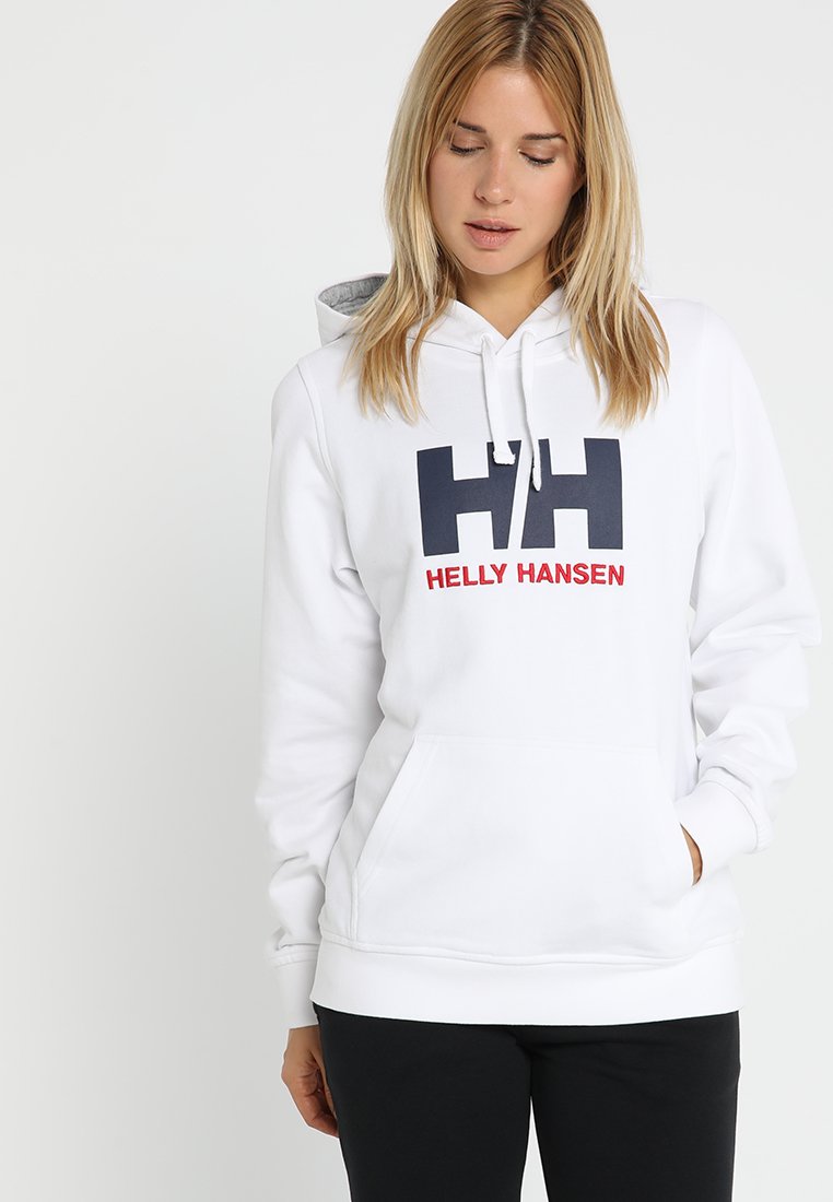 Bílá mikina s kapucí vyrobená z měkké tkaniny, zdobená velkým námořnickým logem "HH" a nápisem "HELly HANSEN" v červené barvě. Obsahuje přední kapsu a stahovací kapuci.