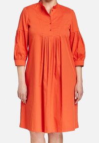 Vestito di cotone arancione con colletto alla mandarina con bottoni, maniche a sbuffo 3/4 e un design frontale plissettato. Texture liscia, silhouette alla lunghezza del ginocchio.