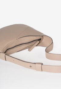 Beige leren schoudertas met een ritssluiting aan de bovenkant en een verstelbare strap, gefotografeerd op een witte achtergrond.