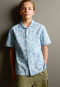 Kurzärmeliges Hemd mit Knopfleiste aus hellblauem Stoff mit wiederholtem Smiley-Gesichtsmuster, mit lockerem Schnitt und klassischem Kragen.