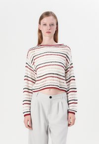 Crochet sweater with red, black, and beige stripes, featuring a loose fit and cropped length. Paired with light grey high-waisted trousers.