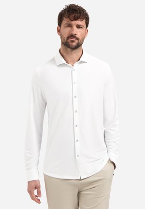 Wit overhemd met lange mouwen en een puntige kraag, voorzien van knoopsluiting en een gladde textuur. Draagt lichtbeige broek erbij.