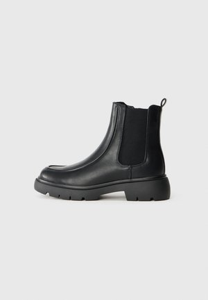 Bottines en cuir noir avec des panneaux élastiques sur les côtés, bout rond et semelle en caoutchouc épaisse avec un motif de grip texturé.