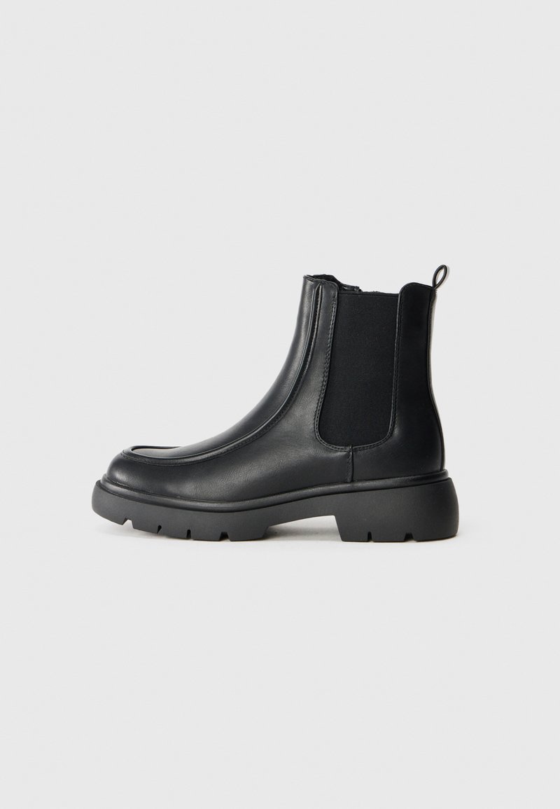 Botines de cuero negro con paneles de elastano en los lados, puntera redondeada y suela de goma gruesa con un patrón de agarre texturizado.