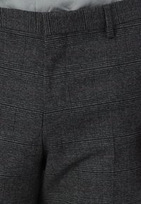 Pantalons à carreaux gris en tissu texturé, ornés de fines lignes rouges, coupe slim, et taille plate pour une apparence ajustée.