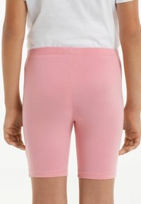 Svetle růžové strečové bavlněné šortky se středním pasem, s hladkým povrchem a jednoduchým zakončením. Zobrazeno ze zadní strany.