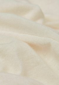 Cremfarbener, strukturierter Stoff mit einer weichen, glatten Oberfläche und sichtbarem Strickmuster, das in sanften Falten fällt. Keine ausgeprägten Muster oder Akzente.