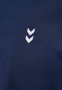 Tessuto blu navy con una trama texturizzata e un design grafico bianco di due chevron rivolti verso il basso sul lato sinistro.