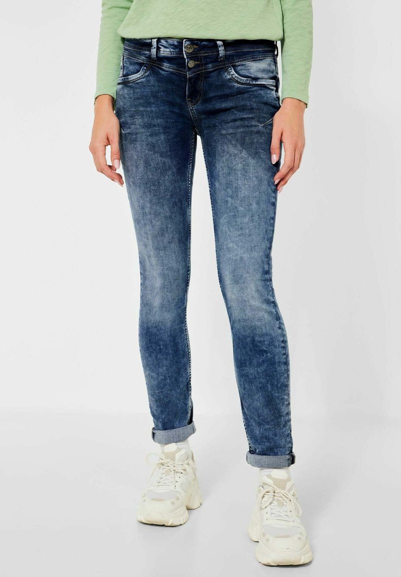 Hubené modré džíny s vybledlým praním, zapínání na dva knoflíky, přední kapsy a ohrnuté nohavice, kombinované s bílými teniskami.