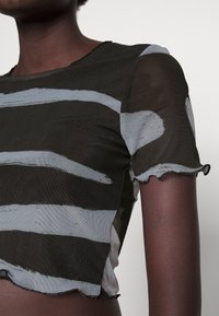 Svart nätcrop top med vita penseldragmönster, scalloped ärmar och kanter med en texturerad finish.