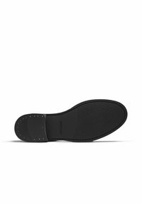 Black shoe sole with textured surface and smooth accents; features a rubber material and small gold studs near the heel.