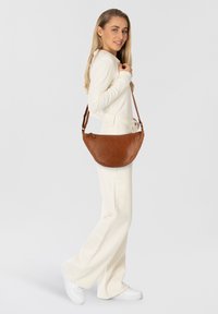 Borsa a tracolla in pelle marrone con forma curvata, tracolla regolabile, texture liscia e branding sottile sul davanti.