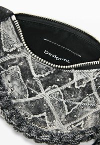 Čierna a sivá vzorovaná listová kabelka s textúrovanou látkou, korálikovými ozdobami a pleteným okrajom. Zapínanie na zips s vnútornou štítkom s logom.