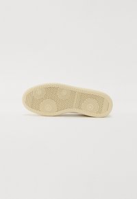 Beige sneakersål med sirkulære og teksturerte mønstre; glatt materiale; avrundet form; inkluderer horisontale riller for grep.