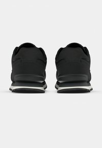 Mustat urheilukengät, joissa on sileä tekstiilipinta, pehmustettu harmaa-musta pohja ja minimalistinen muotoilu, ilman näkyviä logoja.