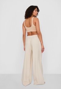 Bralette beige aderente con spalline larghe abbinato a pantaloni larghi, leggeri, beige chiaro, a coste e con vita alta e elastico.