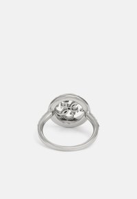 Silverring med ett cirkulärt mönster och en utklippt logotyp i mitten, texturerad band, polerad yta och släta kanter.
