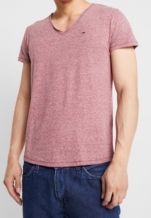 T-shirt rouge en jersey à manches courtes et décolleté en V, fabriqué dans un tissu doux, avec un petit logo sur la poitrine et une coupe décontractée. Porté avec un pantalon en denim bleu.