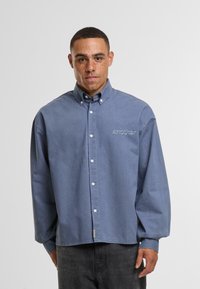 Camicia button-up azzurro chiaro con colletto, dotata di maniche lunghe e logo ricamato sul petto. Realizzata in tessuto morbido con vestibilità comoda.