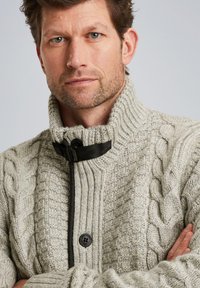 Maglione lavorato a maglia di colore grigio chiaro con colletto alto, caratterizzato da motivi a treccia, un bottone nero e una fascia regolabile al collo.