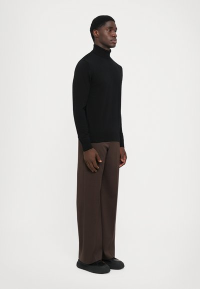 Pulover negru cu guler înalt, cu o croială slim, asortat cu pantaloni largi de culoare maronie, purtat cu pantofi negri slip-on. Textură netedă, design minimalist.