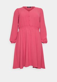 Rosa klänning med V-urringning, långa ärmar och elastisk midja. Har knappar längs fronten och en flödande kjol. Mjuk tygtextur.