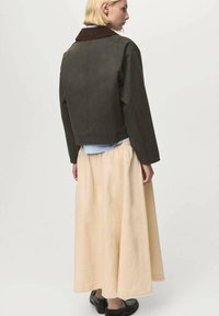 Veste cropped vert foncé avec un col en velours côtelé marron, associée à une jupe beige évasée. Des chaussures noires complètent la tenue.