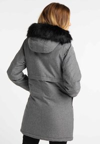 Manteau long gris en tissu texturé, avec une capuche amovible en fausse fourrure noire et une taille cintrée.