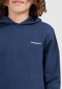 Navyblauwe hoodie gemaakt van zachte stof; heeft een klein wit "BALLIN'" logo op de borst en een relaxte pasvorm.
