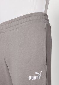 Grijze joggingbroek van zacht materiaal, met een elastische tailleband en een wit geborduurd Puma-logo op het onderbeen.