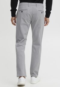 Pantalones grises con una textura sutil, diseño de pierna recta, dos bolsillos traseros con botones, combinados con zapatillas blancas.