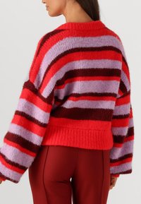 Rood en paars gestreepte gebreide trui met brede mouwen, geribbelde zoom en zachte textuur. Gecombineerd met aansluitende rode broek.