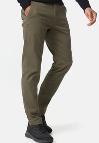 Pantalones verde oliva hechos de una tela suave con corte ajustado, que cuentan con bolsillos laterales y un diseño frontal plano. Llevados con zapatillas negras.