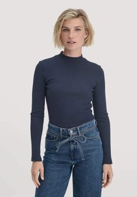 Navyblaues langärmeliges, figurschmeichelndes Oberteil mit hohem Kragen, aus geripptem Stoff, kombiniert mit hoch taillierten blauen Jeans aus Denim mit einer Krawattenbund-Detail.