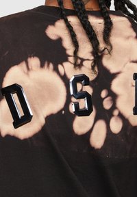 Černé tričko se vzorem tie-dye s výraznými, lesklými písmeny "D" a "S" v kontrastních barvách. Bavlněný materiál s jemnou strukturou.