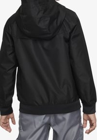 Musta hupullinen takki, jossa on sileä pinta, joustavat hihansuut ja vyötärönauha. Helppo muotoilu ilman näkyviä logoja tai somisteita.